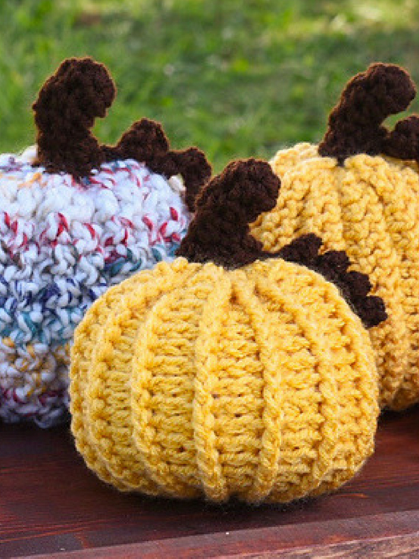 Three crocheted pumpkins on a wooden table.