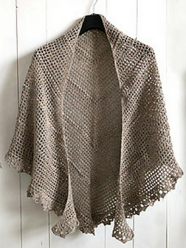 A beige crocheted shawl hanging on a wooden wall.