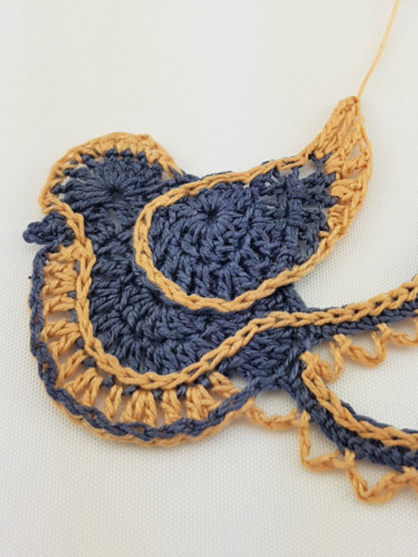 A festive blue and yellow crocheted bird on a white surface.
