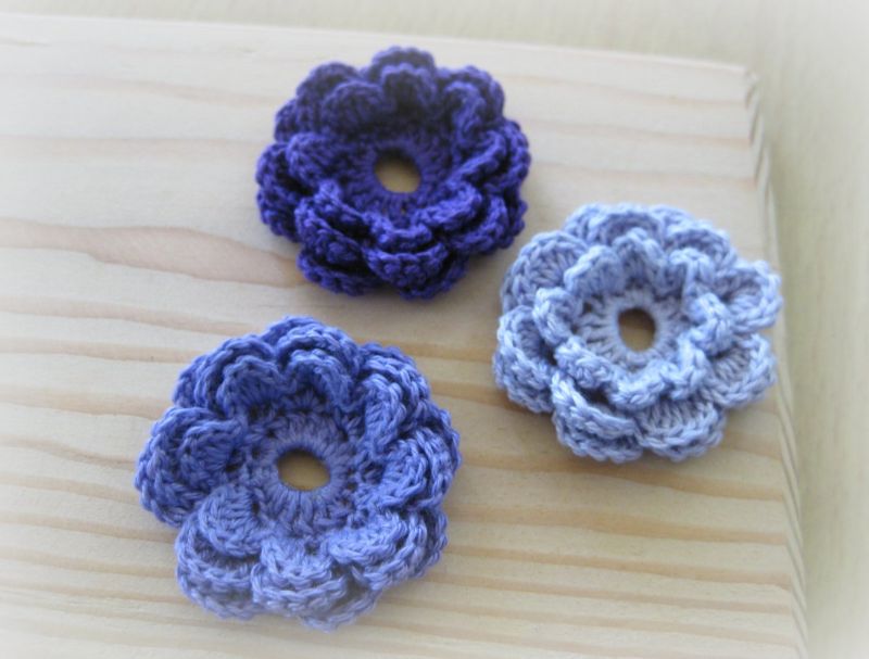 Three crochet flowers on a wooden table.
