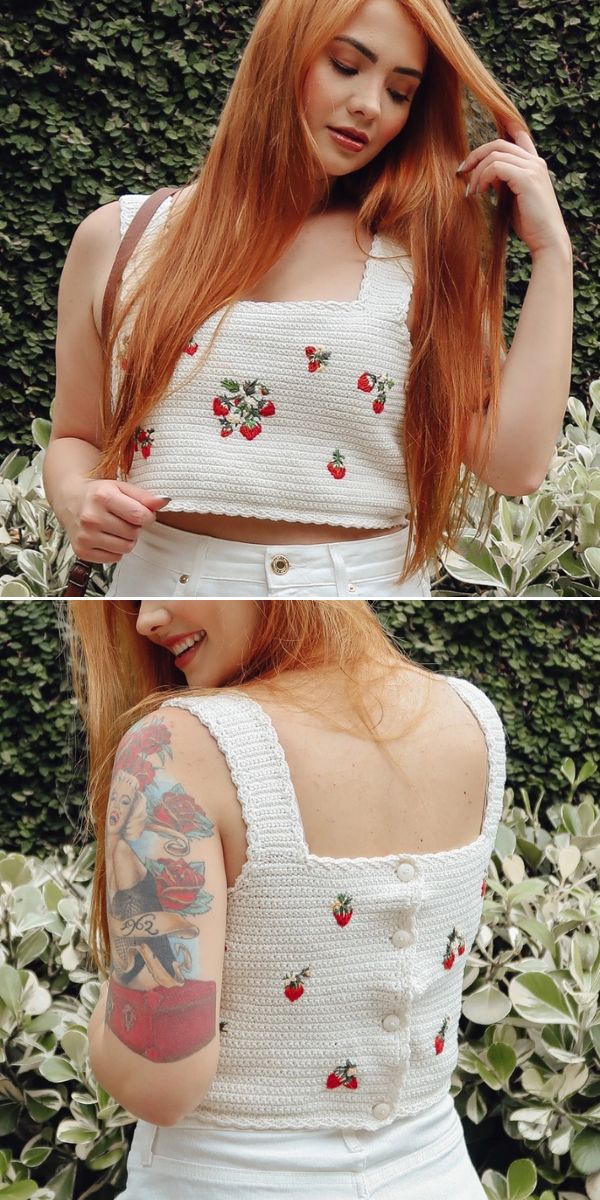 A woman with long red hair wears a crochet crop top with small strawberry designs and buttons down the back, paired with high-waisted white pants.