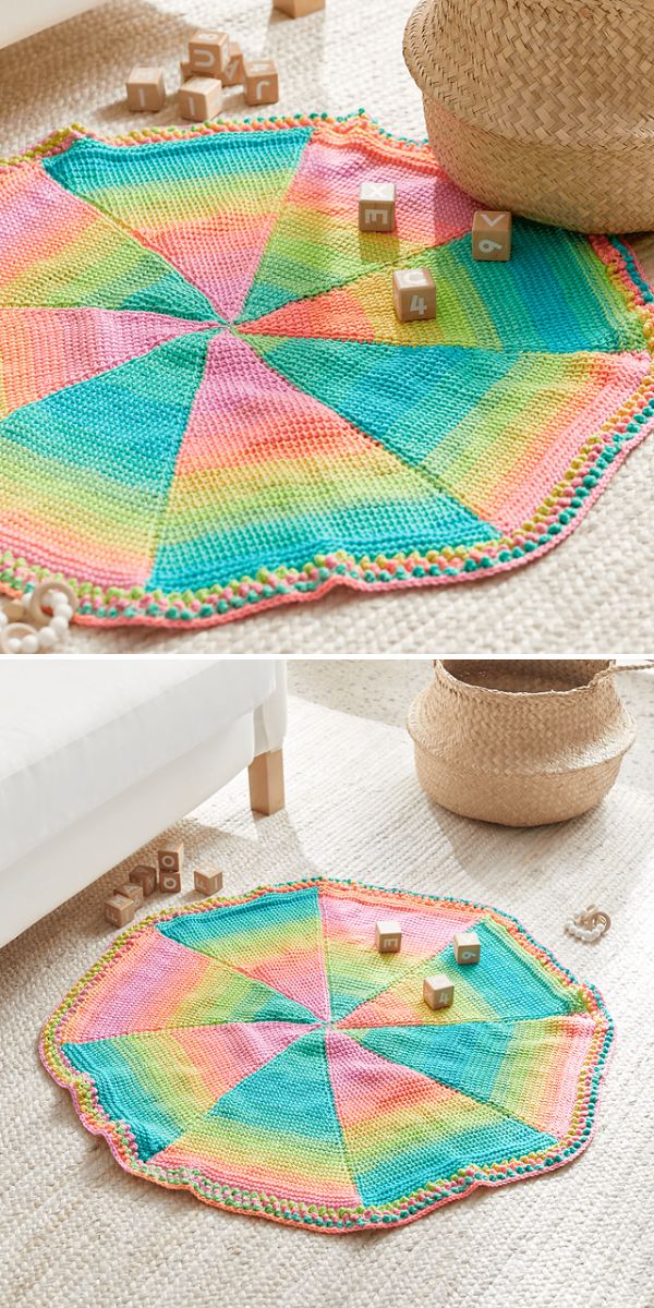 Round, multicolored knitted play mat with pastel rainbow segments is spread on a light carpeted floor, surrounded by wooden letter blocks and a woven basket filled with free crochet patterns for baby dresses.