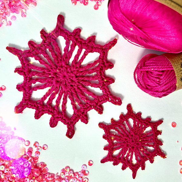 Two pink crocheted snowflakes on a white surface.