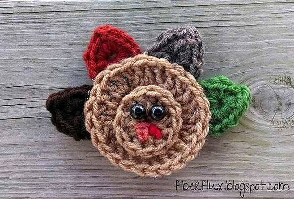 A crocheted turkey brooch on a wooden surface.