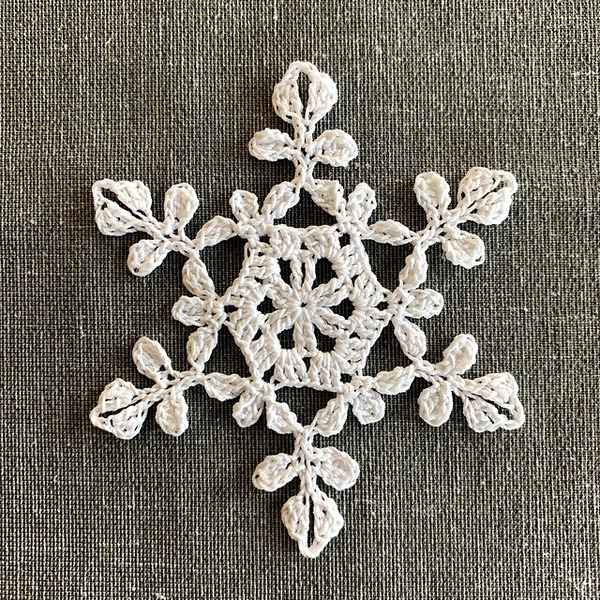 A white crochet snowflake on a gray fabric.