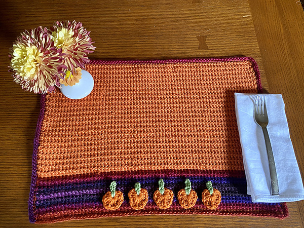 A crocheted pumpkin placemat on a table.
