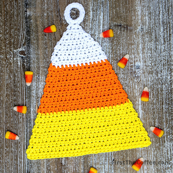 A crocheted candy corn pot holder on a wooden table.