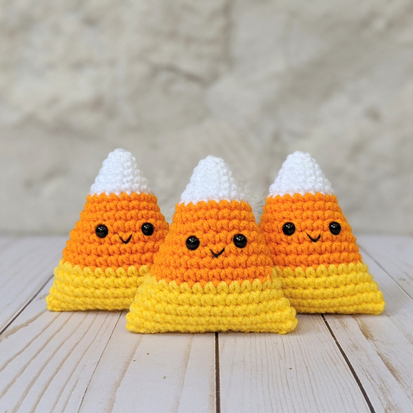 Three crocheted candy corn amigurumi on a wooden table.
