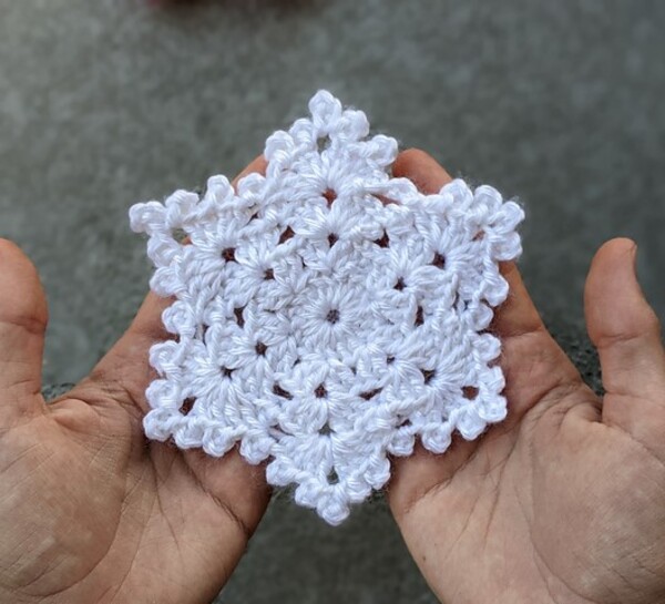 A person holding a crocheted snowflake.