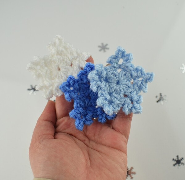 Three crochet snowflakes in a person's hand.