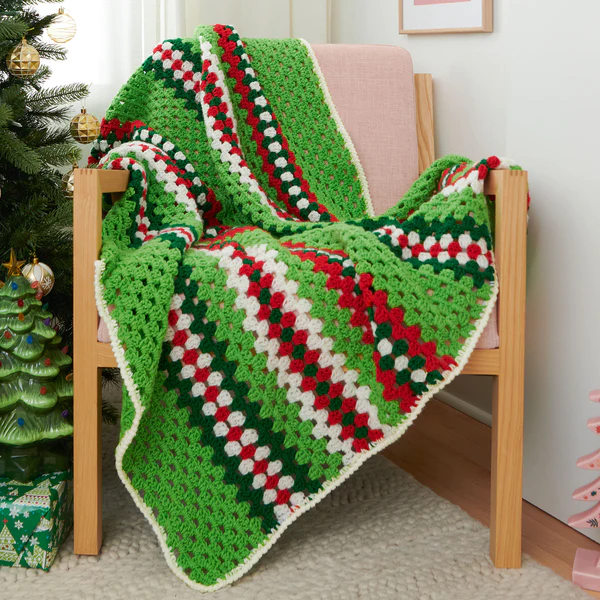 A green and white crocheted afghan in front of a christmas tree.