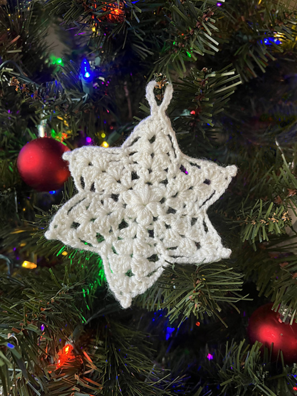 A crocheted star ornament hanging on a christmas tree.