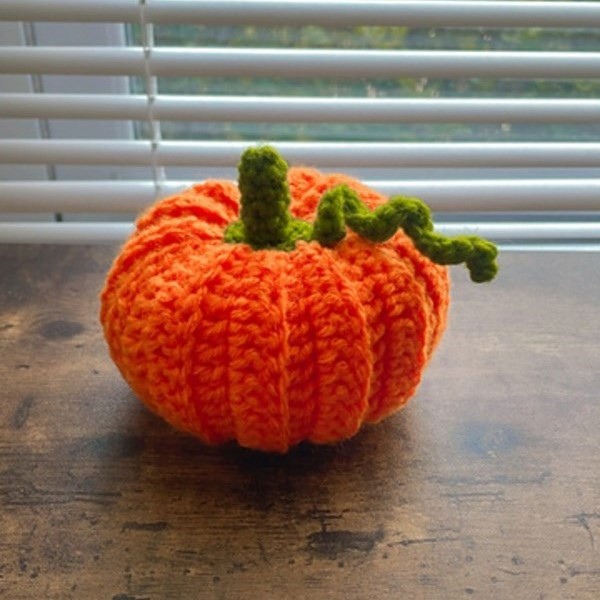 A crocheted pumpkin sitting on a wooden table.