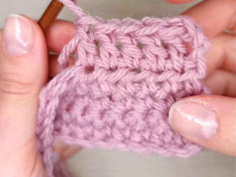 Hands crocheting pink yarn with a double crochet hook.