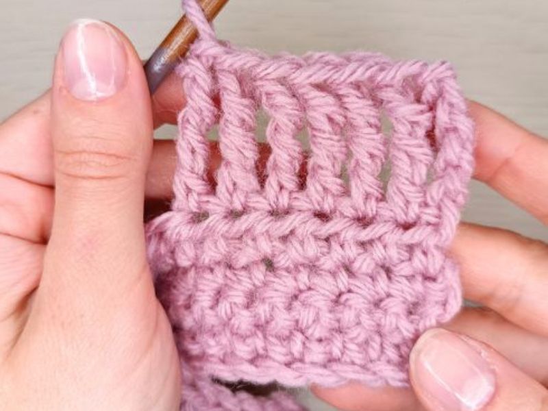 Close-up of hands crocheting pink yarn with a crochet hook.