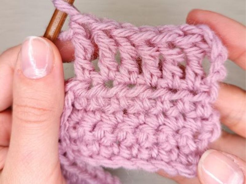 Close-up of hands holding a pink crochet project and a crochet hook.