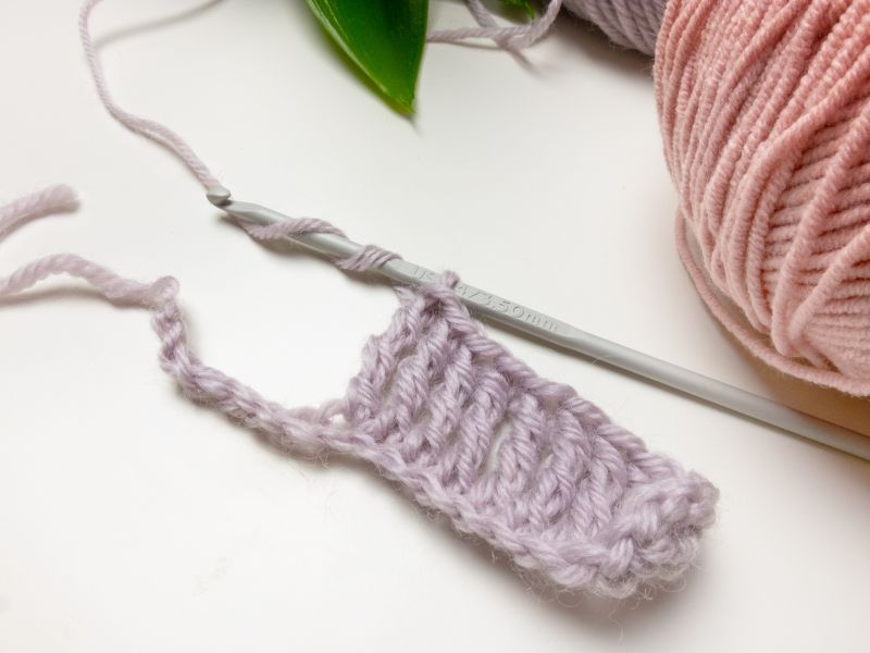 A small piece of purple crochet work with a crochet hook and strands of yarn on a white surface.