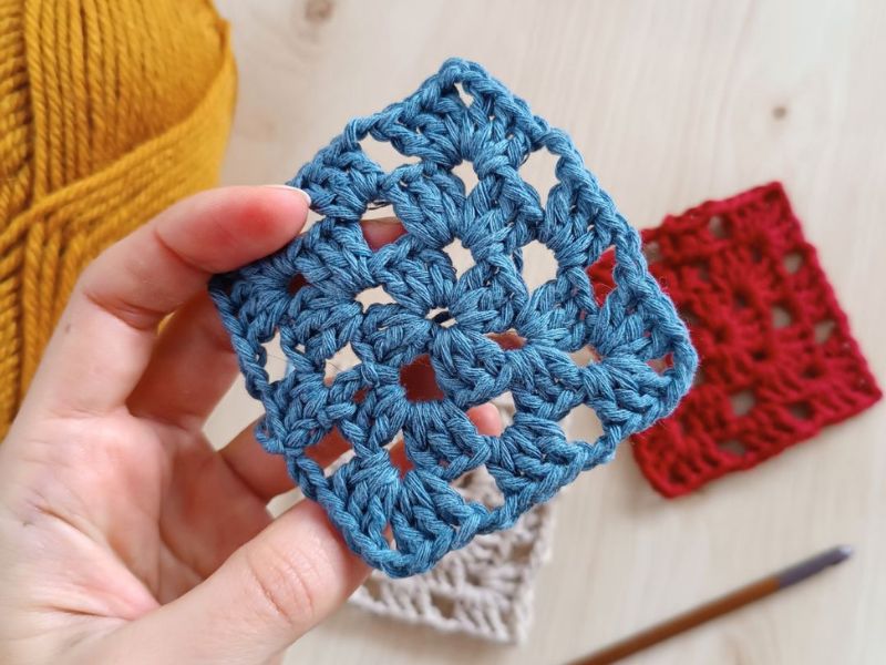 a person holding a crochet granny square