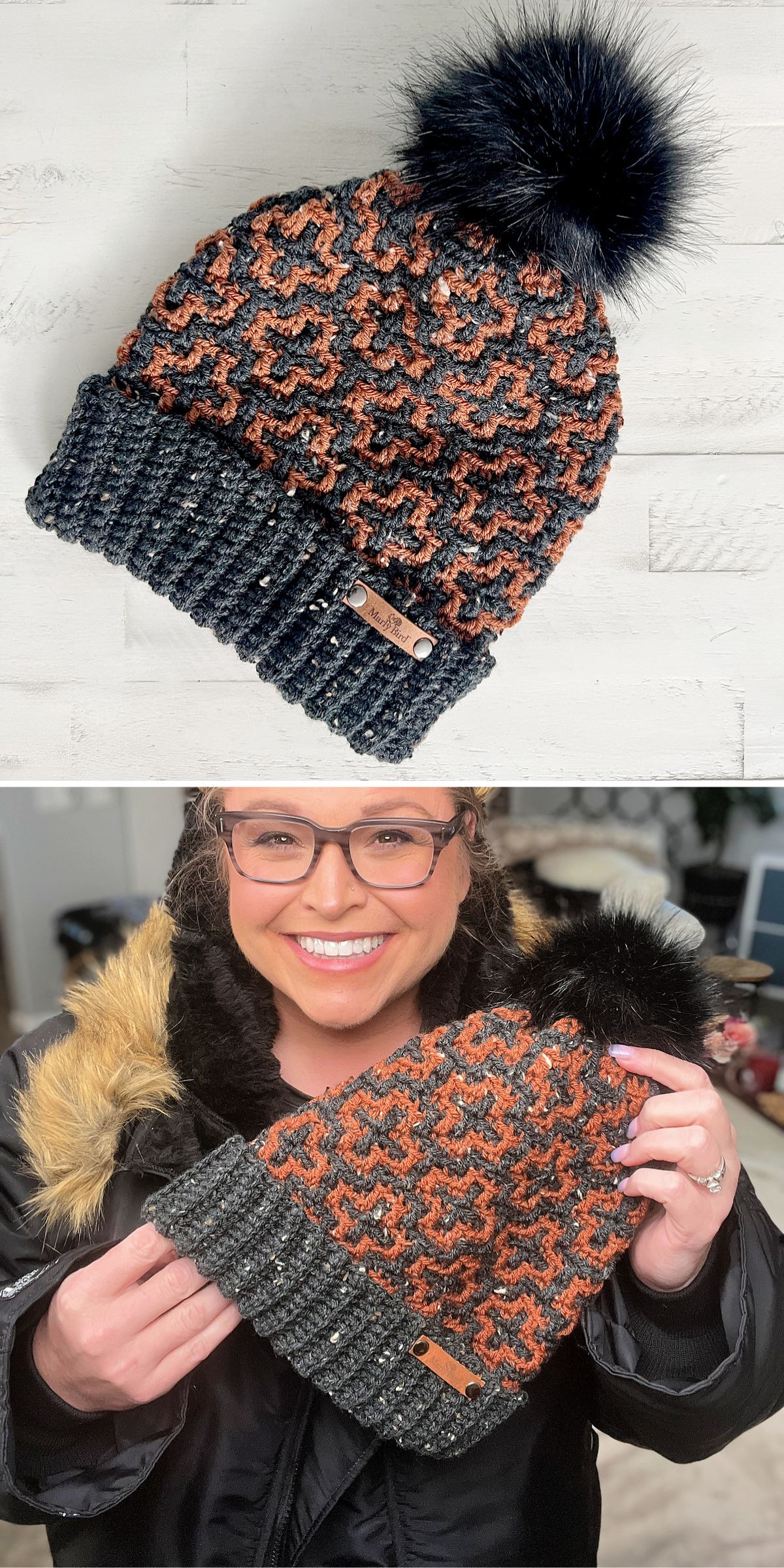 A crochet hat with a geometric pattern and a large pom-pom, held by a person wearing glasses and a winter coat with a fur-lined hood.