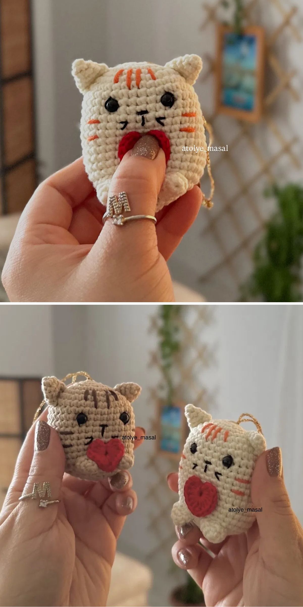 Two hands display small crocheted cat keychains with red hearts, photographed indoors against a blurred background with wooden decor and a plant.