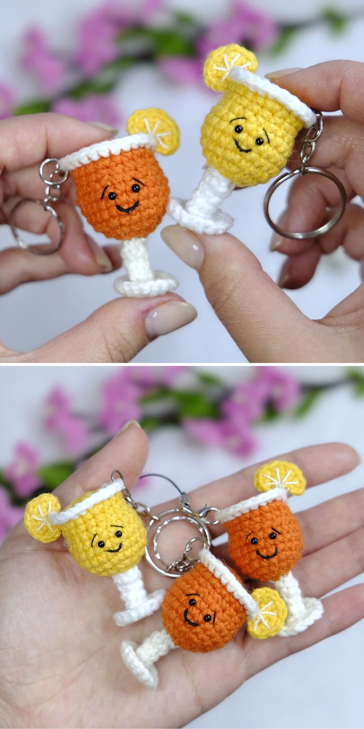 Two hands holding crocheted keychains shaped like smiling orange and yellow drinks in cocktail glasses, each with a lemon or orange slice, against a blurred floral background.