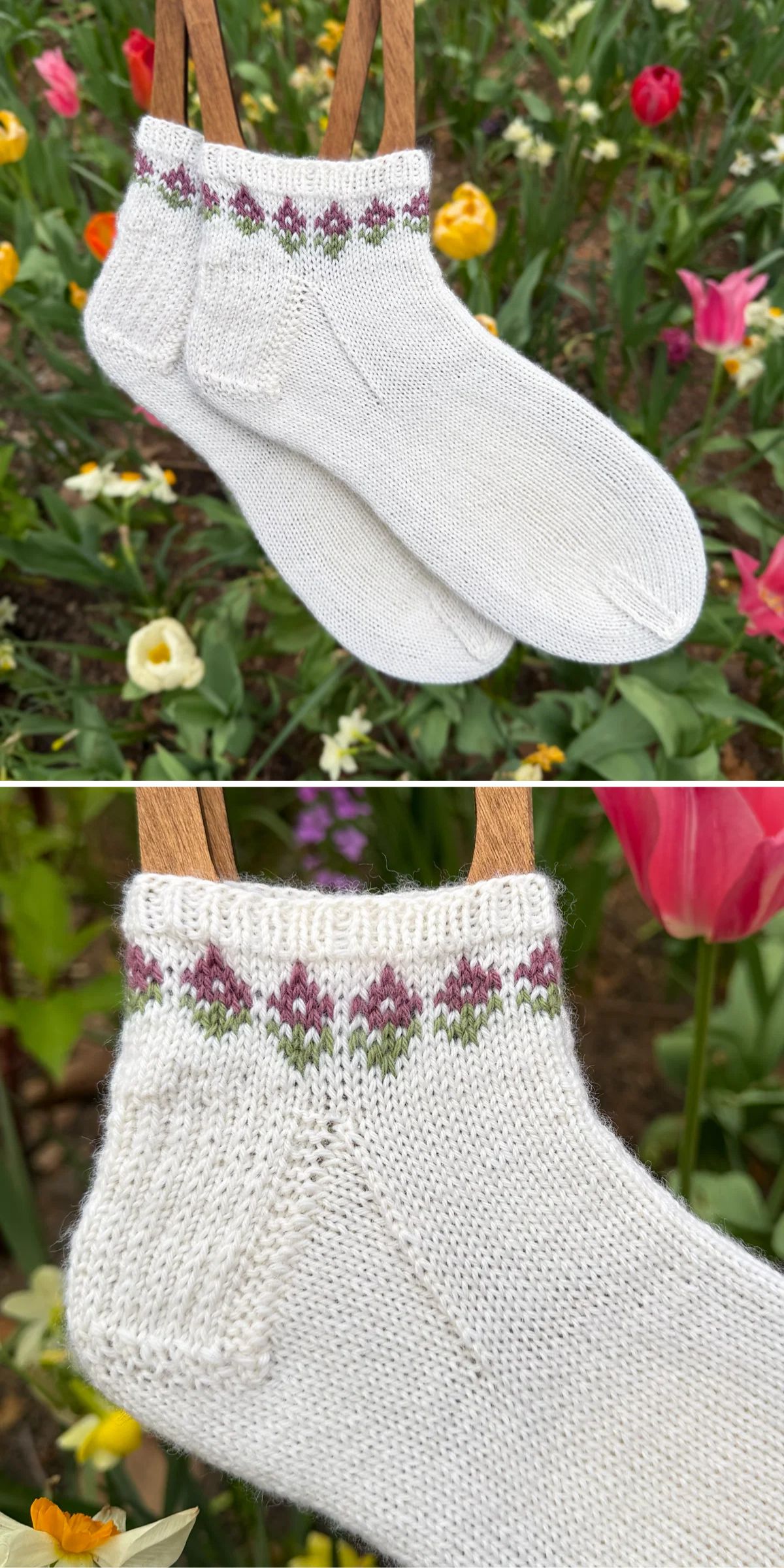 Two white knit socks with a purple and green floral pattern near the cuff are displayed outdoors with blooming tulips in the background.