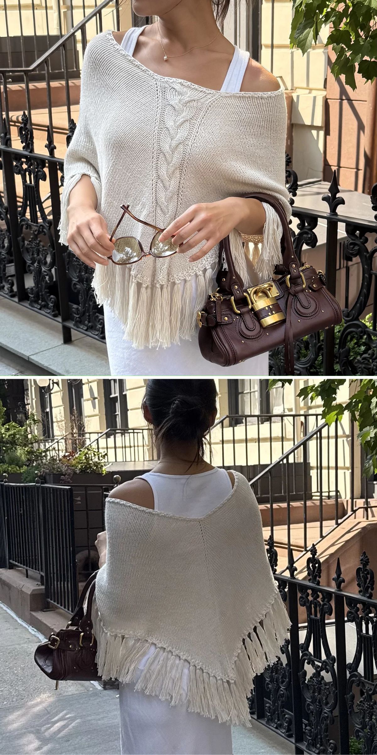 A woman in a white dress and fringed knit shawl holds sunglasses and a brown handbag while standing on a city sidewalk near a black iron fence.