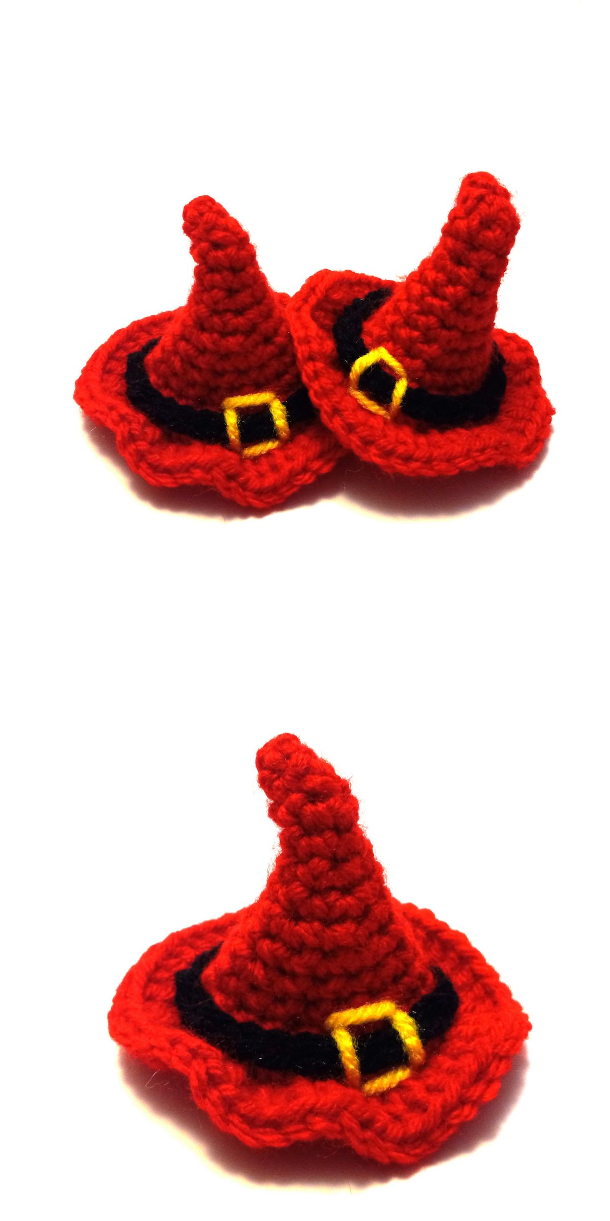Three small, crocheted red witch hats with black bands and yellow buckles are shown on a white background. Two hats are grouped together and one hat is separate.