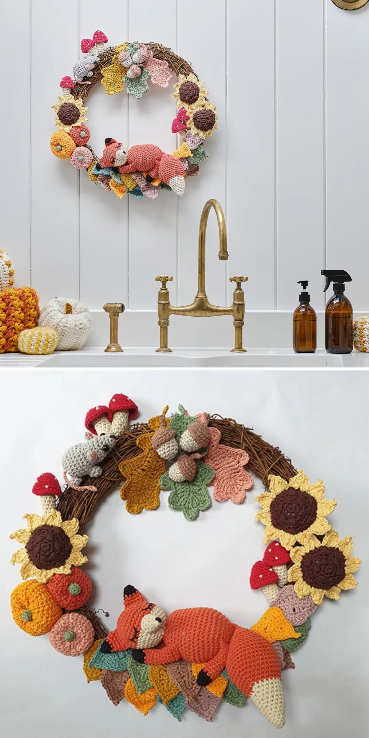 A crocheted wreath with sunflowers, mushrooms, and a fox is hung above a brass sink with soap dispensers in a white bathroom.