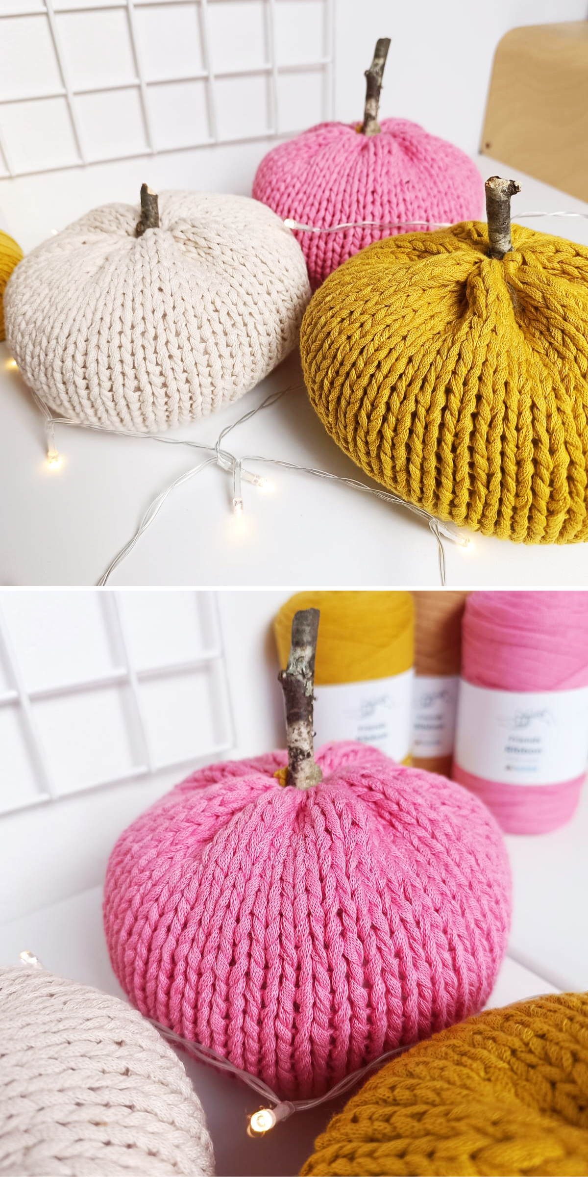 Three knitted pumpkins in cream, yellow, and pink colors with stick stems are displayed on a white surface with yarn spools and string lights in the background.
